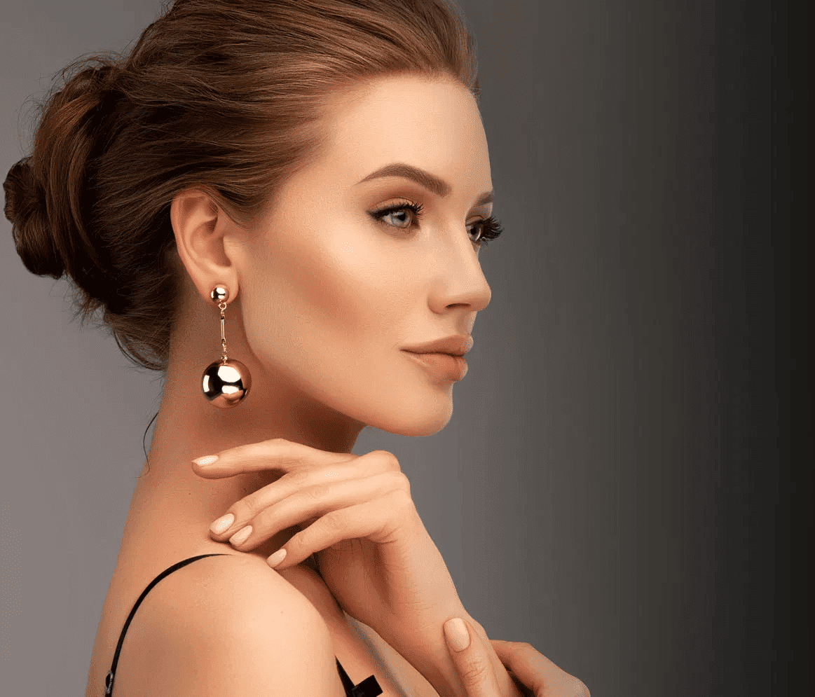 Elegant woman with updo hairstyle wearing gold earrings, looking thoughtfully to the side.